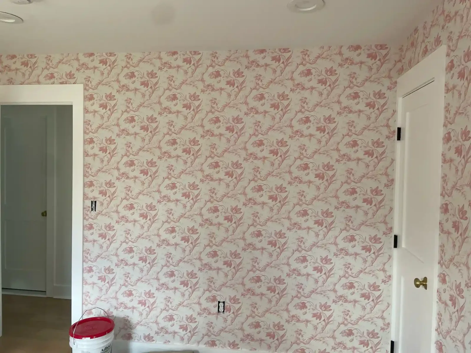 Pale wallpaper with a repeating pink floral motif in a room corner